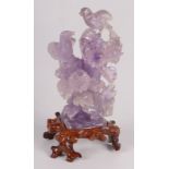 A Chinese amethyst carving of a pair of birds perched on a flowering and leafy tree stump,
