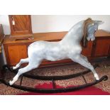 A grey rocking horse on a black painted wood stand, height 123cm, width 183cm, depth 47cm.