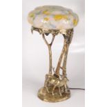 A gilt bronze table lamp, early 20th century, with mottled glass shade above trees and a deer,