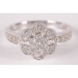 A 9ct white gold flower head diamond cluster ring with diamond set shoulders.