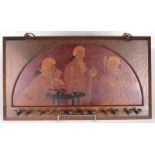 An Arts and Crafts oak pipe rack, depicting three gentlemen smoking, with six racks, height 32cm,