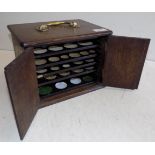 An oak coin cabinet, the double doors open to reveal 5 of 11 drawers with brass swing handle,