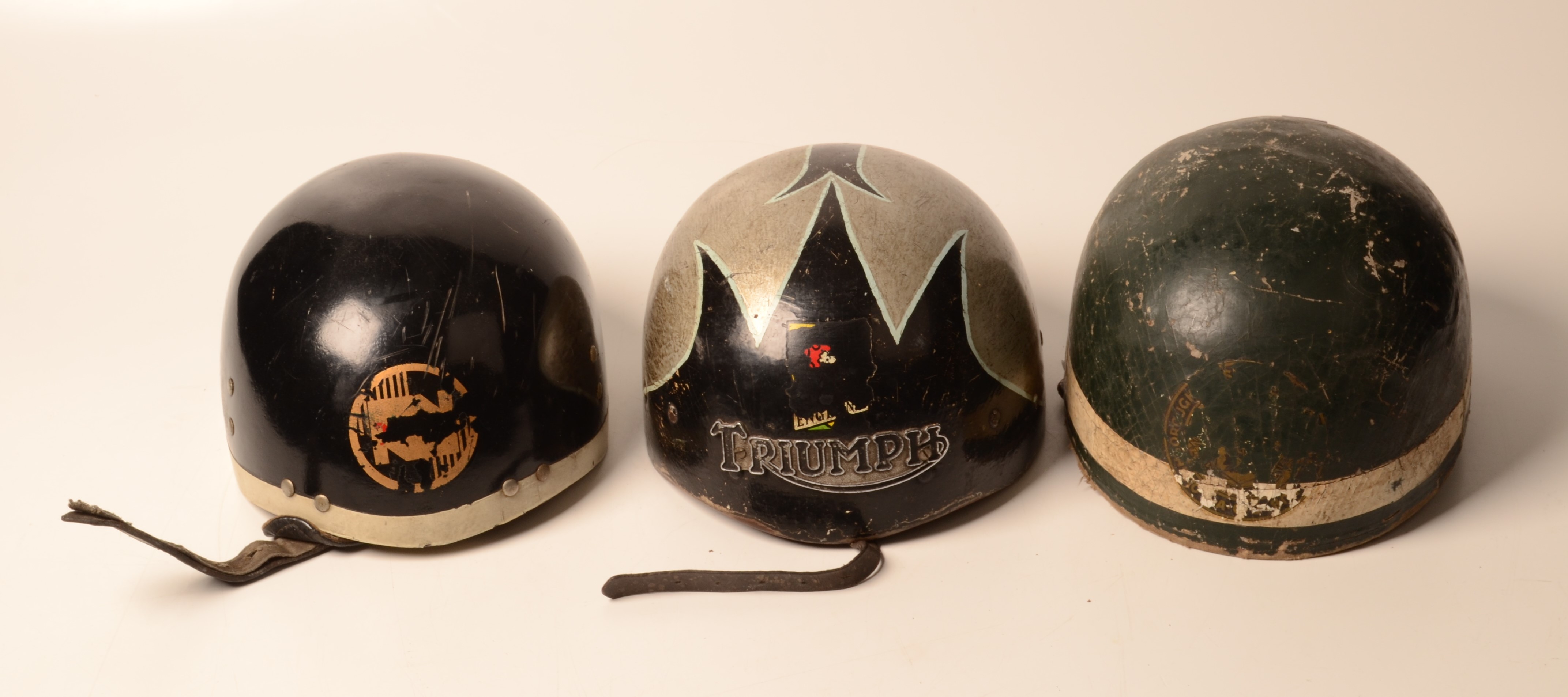 A Triumph wooden motorbike helmet and two others.