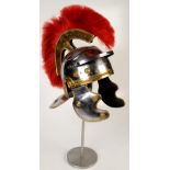 A reproduction white metal and brass Roman helmet, with a red brush, on metal stand,