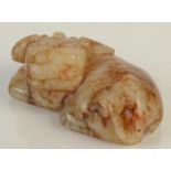A Chinese white and brown striated jade pebble carved as a reclining Buddhist Dog of Fo,