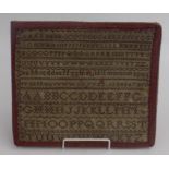 A needlepoint alphabet sampler, 19th century, framed within the cover of a blotter, 26 x 28.5cm.