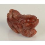 A Chinese cream and red mottled soapstone pebble carved as a reclining Buddhist lion dog,