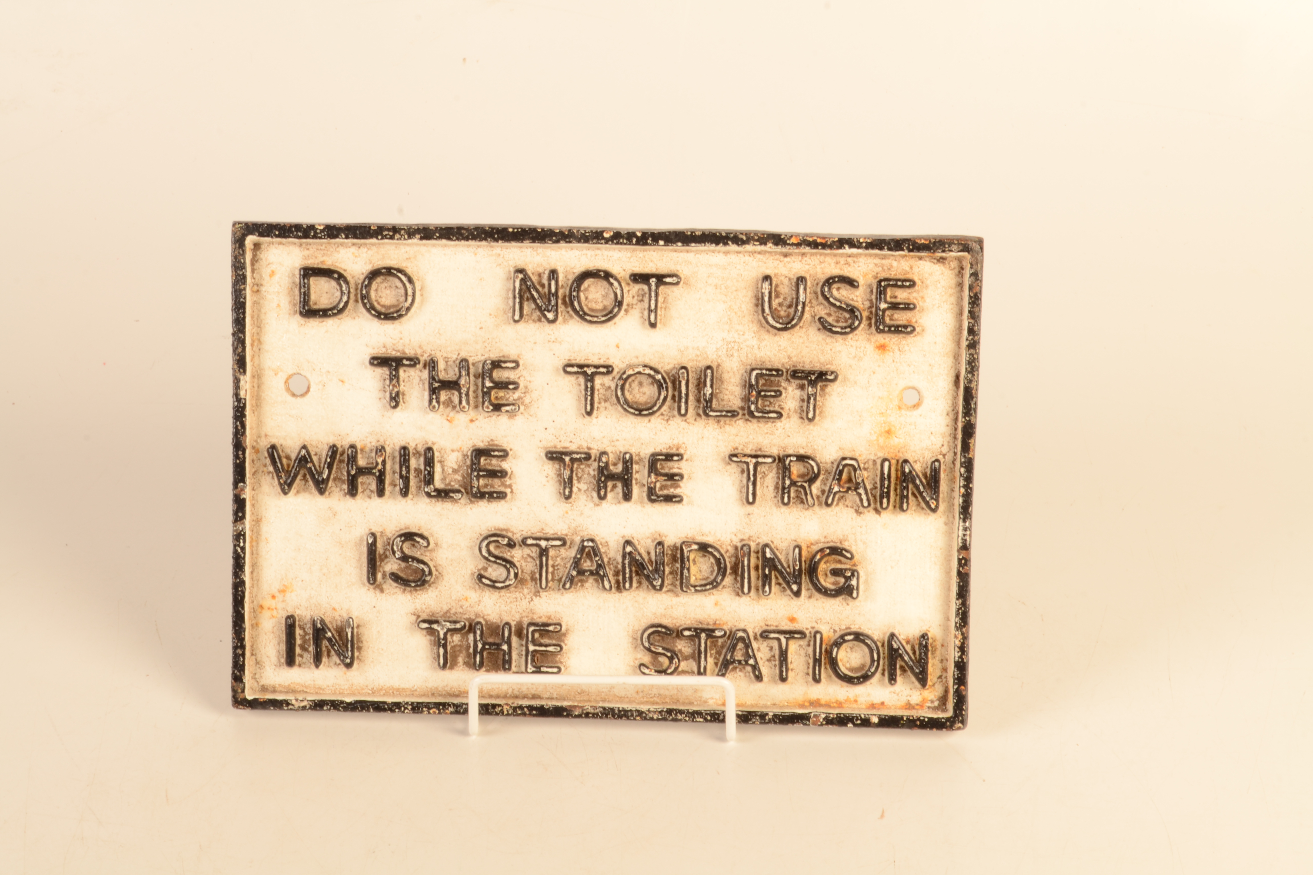 A cast iron painted sign, 'DO NOT USE THE TOILET WHILE THE TRAIN IS STANDING IN THE STATION,