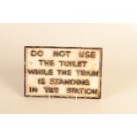 A cast iron painted sign, 'DO NOT USE THE TOILET WHILE THE TRAIN IS STANDING IN THE STATION,