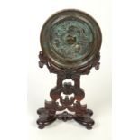 A Chinese bronze circular mirror, on carved hardwood stand, diameter of mirror 10.