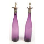 A pair of amethyst glass wine bottles with silver tops decorated with vine leaves.