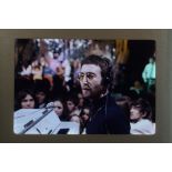 An original 35mm transparency of John Lennon seated in front of a piano at a concert.