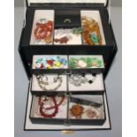 Costume jewellery in a black multi compartment jewel chest.