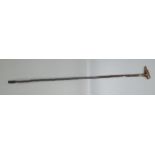 A walking cane, with a carved wooden handle in the form of a greyhound's head wearing a hat,
