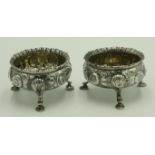A pair of Georgian ornate silver salts with floral repousse decoration and gadrooned borders,