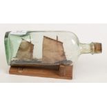 An early model of a St Ives fishing boat in a bottle on a wooden stand, length of bottle 23cm.