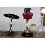 A cranberry glass oil lamp with brass column together with a brass and painted metal trivet (2)