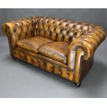 A 2 seat Chesterfield upholstered in brown buttoned leather, raised on bun feet 74cm h x 160cm w x