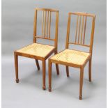 A pair of Edwardian mahogany stick and rail back bedroom chairs with woven cane seats, raised on
