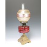 A Victorian cranberry glass oil lamp reservoir raised on a pierced gilt framed iron base and with