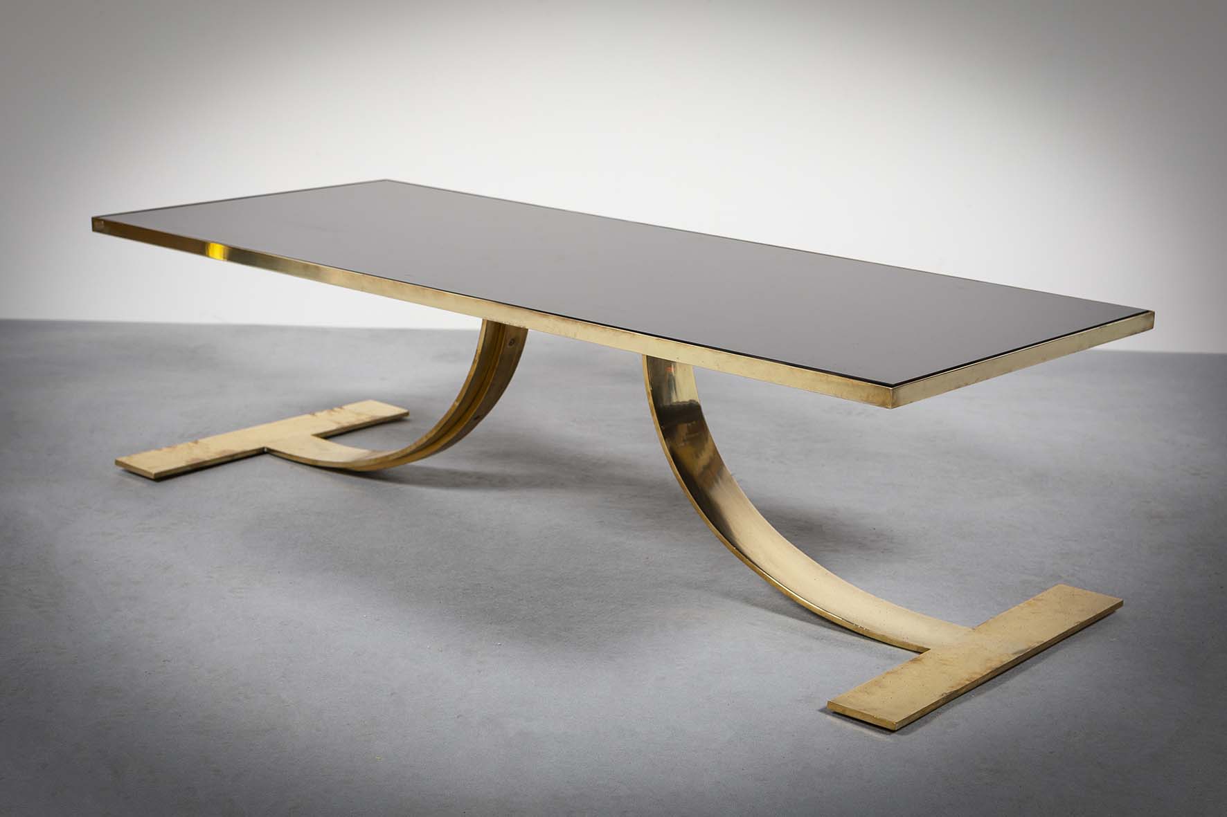 A RECTANGULAR LOW TABLE, 1970s, with black glass inset top, on a splayed gilt base, 120cm x 51cm x