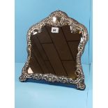 A LATE VICTORIAN EMBOSSED SILVER FRONTED EASEL MIRROR of cartouche form decorated with flower heads