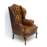 A late 20thC leather button back winged library chair with brass stud detailing and standing on