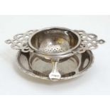 A silver plate tea strainer on stand.