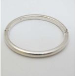 A white metal bracelet of bangle form .