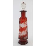 A ruby glass flask with etched fruiting vine decoration and clear glass stopper.
