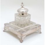 A silver plate Standish of squared form with pen rests and large central cut glass inkwell .