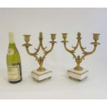 A pair of Continental Empire gilt brass twin branch candelabra on shaped carerra marble squared