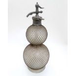 A large glass soda siphon with mesh covering and grip marked 'The Clincher Patent 1365' .