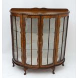 An early / mid 20thC walnut serpentine fronted two door display cabinet with gadrooned top edge and