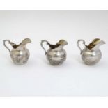 A set of three continental 800 silver small cream jugs with embossed floral and bow decoration.