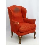 A 20thC red upholstered wingback armchair resting on cabriole legs having carved shell motif and