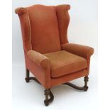 An early / mid 20thC walnut William and Mary style wingback chair with scrolling arms and standing