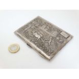 A silver cigarette case having cast decoration to lid depicting a rural Indian like scene with