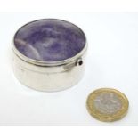 A silver pill box of circular form with amethyst set to lid and red stone cabochon,