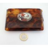A faux tortoiseshell cigarette case with later applied ceramic decoration depicting dog head,