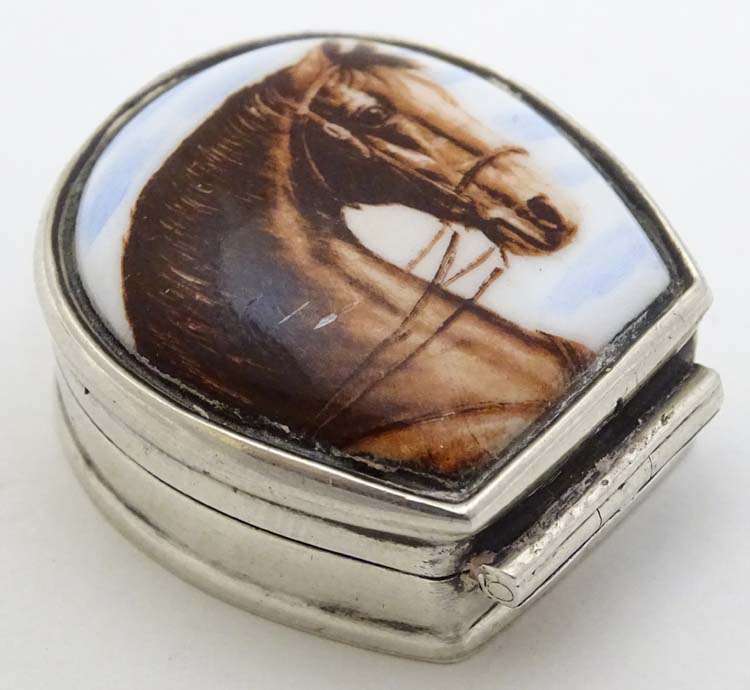 A silver pill box formed as a horseshoe with horse head decoration to top.