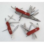 A collection of three Victorinox Swiss army knives, each having a range of blades and tools,