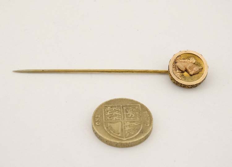 A gilt metal stick pin surmounted by a circular image of a squirrel.