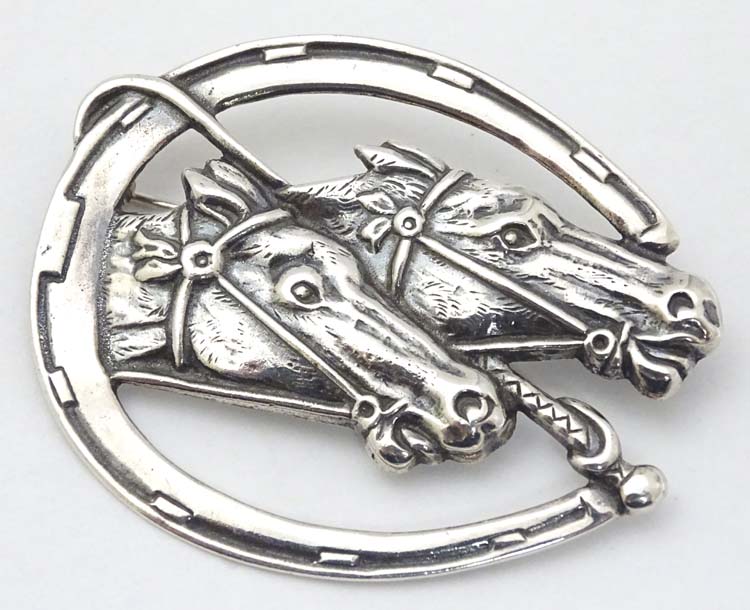 A silver brooch formed as a horseshoe with riding crop / whip and horse head decoration.