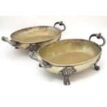A pair of silver plated oval serving dishes with twin handles and standing on acanthus scroll feet.