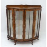 An early / mid 20thC walnut shaped bowfronted two door display cabinet with gadrooned top edge and