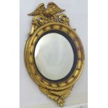 An early 20thC convex mirror with gilt decoration surmounted by an eagle.