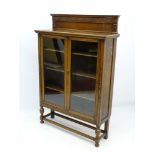 An early 20thC oak glazed bookcase, with a decoratively carved upstand,