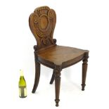 A 19thC mahogany hall chair with a scallop shell decoratively carved backrest and stand on turned