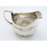 A Geo III silver jug with bright cut decoration, reeded handle and standing on 4 ball feet.